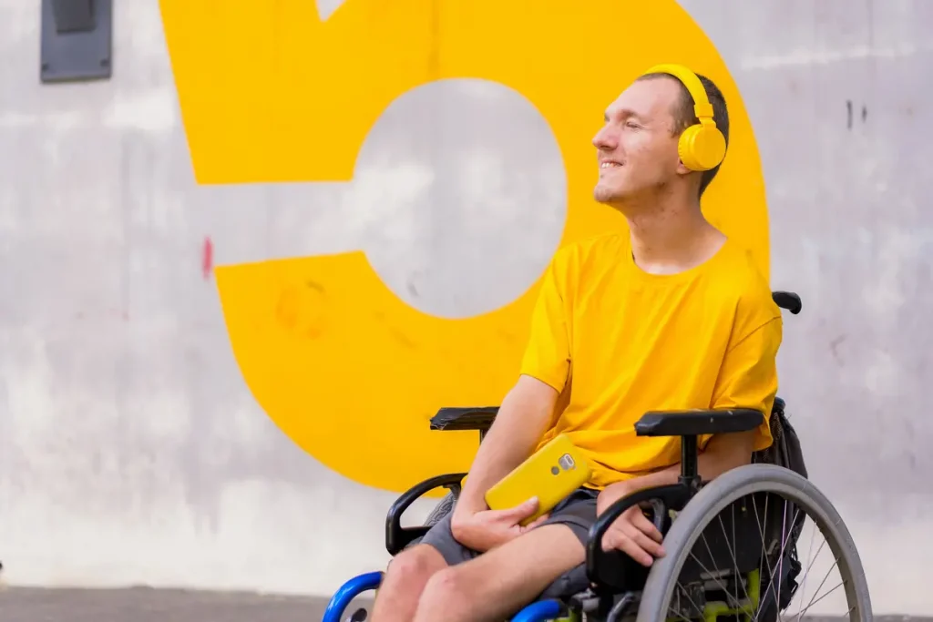 young man in wheelchair dressed in vibrant yellow listening to music in his headphones