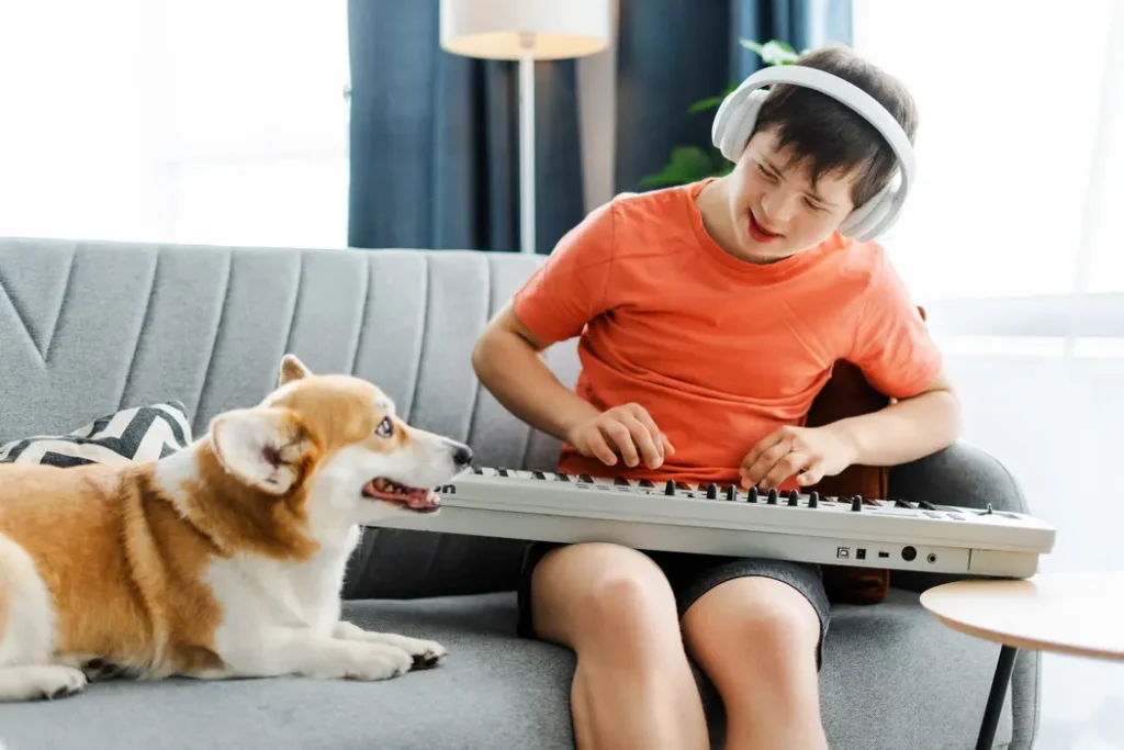 young boy with down syndrome playing an electric keyboard on the couch - he is sitting next to his dog